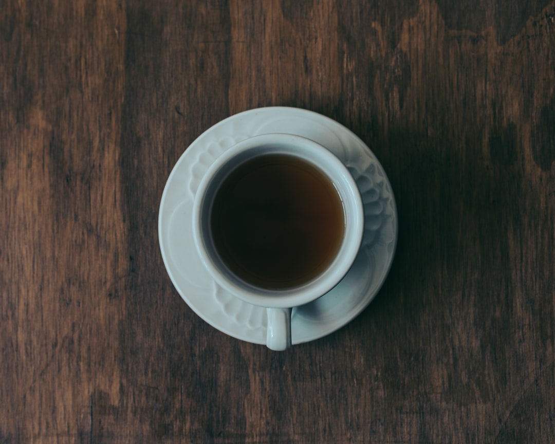 A cup of black tea and a cup of coffee sitting side by side on a wooden table