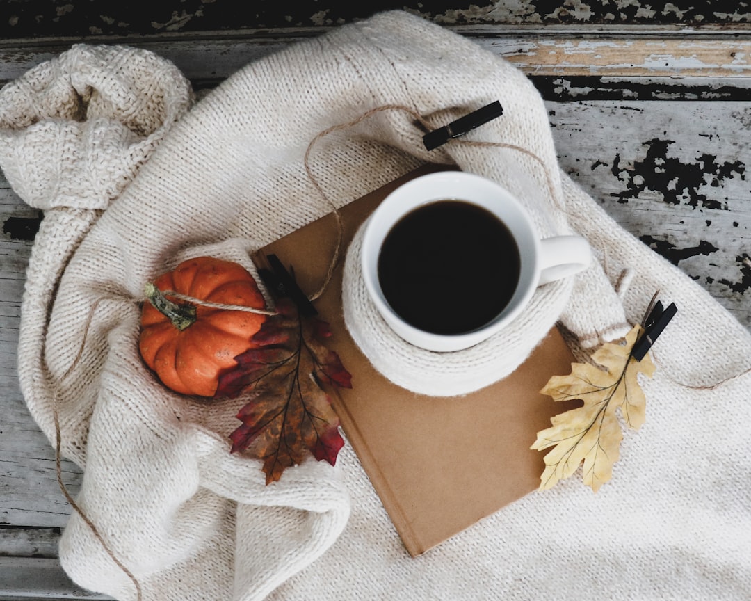 A warm mug of coffee sitting on a wooden table near a window with fall leaves outside